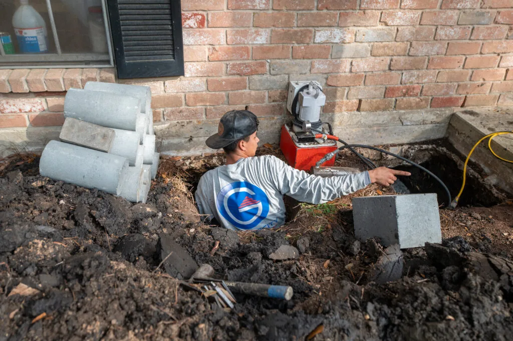 Foundation worker operating hydraulic equipment beside a brick home